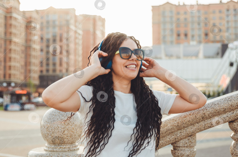 Скачать Молодая жизнерадостная счастливая женщина с дредами, одетая в белую футболку, танцует, слушает музыку в наушниках, отдыхает, расслабляется в городском парке, прогуливается по аллее. Концепция городского образа жизни фотосток Ozero