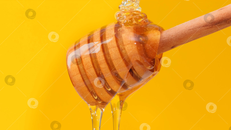 Скачать Крупным планом свежий жидкий мед, льющийся и вытекающий из деревянной ложки-ковшика фотосток Ozero