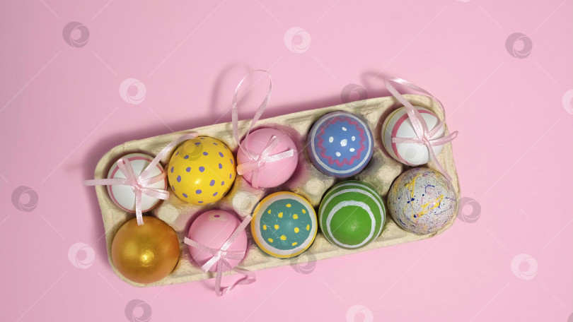 Скачать Разноцветные пасхальные яйца в картонной коробке на розовом фоне. фотосток Ozero