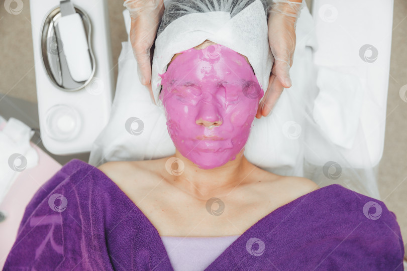 Скачать Заботьтесь о красоте женской кожи. Молодая женщина с альгинатной косметической фиолетовой маской на лице в салоне красоты. фотосток Ozero