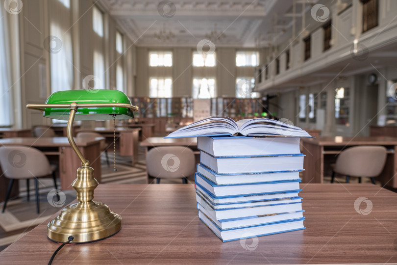 Скачать Стопка книг на деревянном столе и размытая книжная полка в библиотечной комнате. фотосток Ozero
