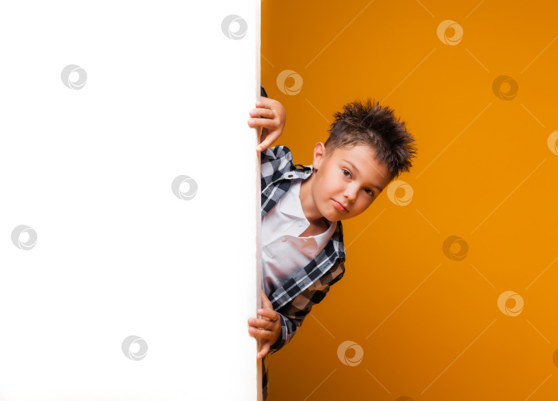 Скачать Улыбающийся мальчик позирует с белым плакатом, глядя в камеру на желтом фоне. Студент рекламирует ваш текст. Макет с пространством для копирования фотосток Ozero