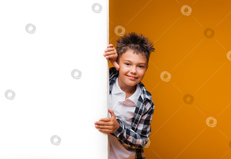 Скачать Улыбающийся мальчик позирует с белым плакатом, глядя в камеру на желтом фоне. Студент рекламирует ваш текст. Макет с пространством для копирования фотосток Ozero