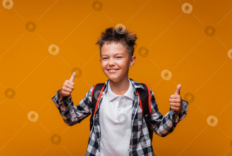 Скачать Обратно в школу. забавный мальчик с рюкзаком в рубашке на желтом фоне демонстрирует супер, класс и улыбается. Смотрит в камеру. место для копирования. Образование. фотосток Ozero