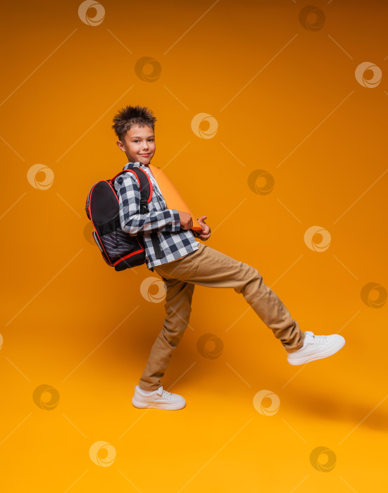 Скачать Вид сбоку на счастливого школьника, улыбающегося и несущего папку, идущего в школу на желтом фоне. портрет школьника. фотосток Ozero