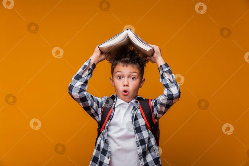 Скачать Портрет мальчика-школьника, держащего книгу над головой, с сумкой, рюкзаком, выделенный на желтом фоне.обратно в школу фотосток Ozero