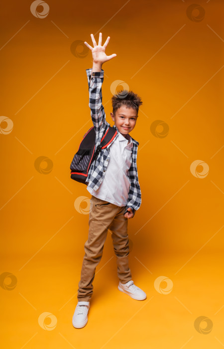 Скачать Студент здоровается на желтом фоне. портрет мальчика с рюкзаком и папкой. фотосток Ozero