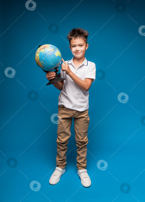 Скачать Улыбающийся маленький мальчик, держащий в руках глобус - изолированный на синем фоне. изучение географии. фотосток Ozero