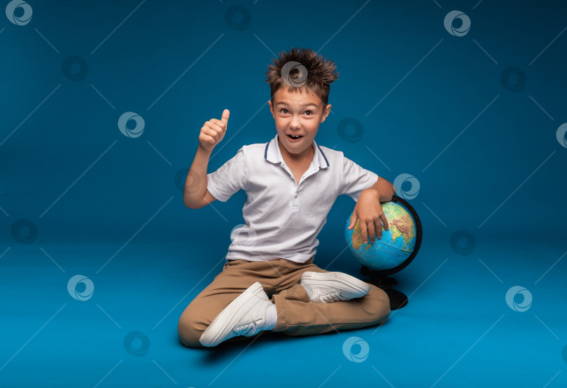 Скачать веселый школьник сидит на синем фоне с рюкзаком и глобусом. концепция образования фотосток Ozero