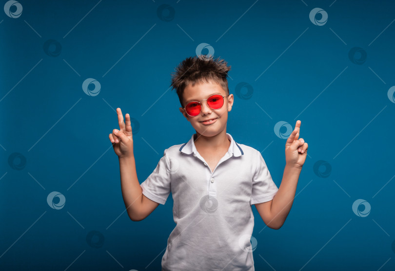 Скачать маленький крутой мальчик, одетый в белую футболку, изображает крутого на синем фоне. портрет мальчика в красных очках фотосток Ozero