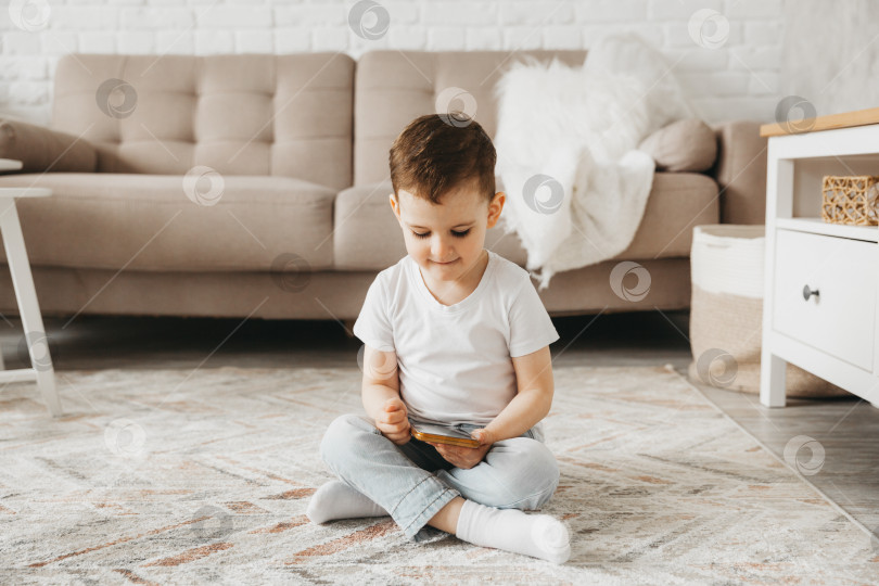 Скачать 5-летний мальчик смотрит на смартфон. ребенок сидит на полу и держит в руках телефон фотосток Ozero