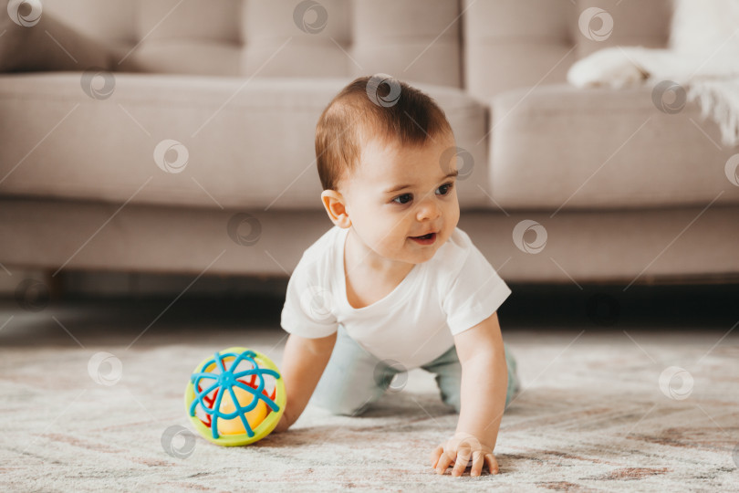 Скачать милый малыш 9 месяцев от роду играет с разноцветным мячом в детской комнате с белой мебелью фотосток Ozero