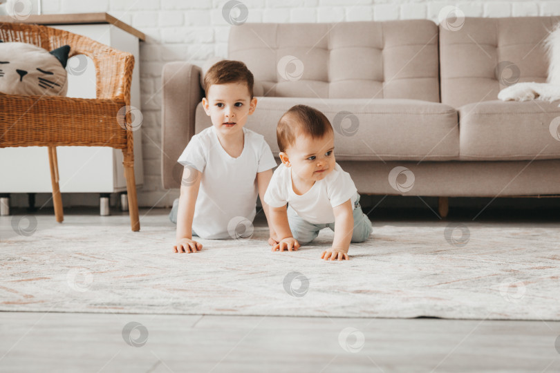 Скачать Два милых малыша в белых футболочках ползают и играют на полу дома. два брата фотосток Ozero