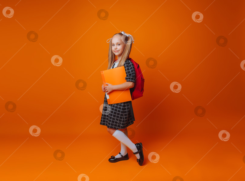 Скачать Обратно в школу. Школьница со школьной сумкой на изолированном желтом фоне студии. маленькая девочка держит в руках папку и рюкзак. фотосток Ozero