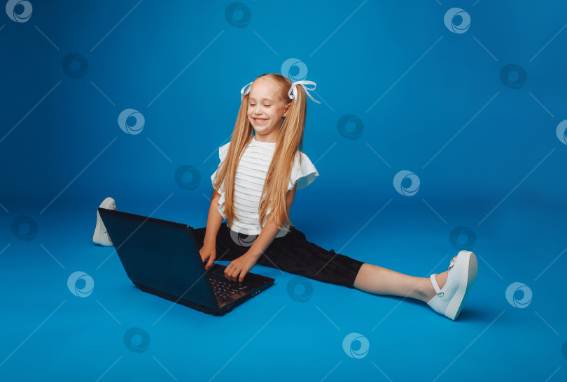 Скачать школьница сидит на синем фоне и смотрит в ноутбук. маленькая девочка учится онлайн. ребенок печатает на ноутбуке. изолированный фон. фотосток Ozero