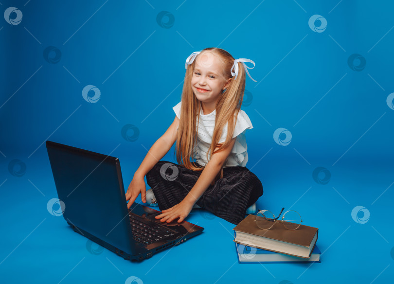 Скачать школьница сидит на синем фоне и смотрит в ноутбук. маленькая девочка учится онлайн. ребенок печатает на ноутбуке. изолированный фон. фотосток Ozero