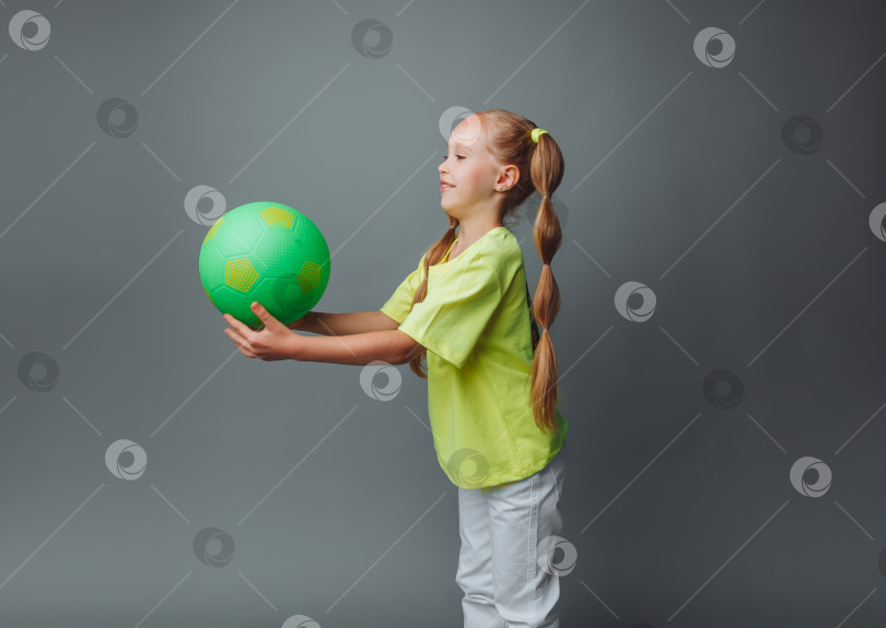 Скачать маленькая девочка подбрасывает мяч вверх, выделяясь на сером фоне. маленький спортсмен.детский спорт. фотосток Ozero