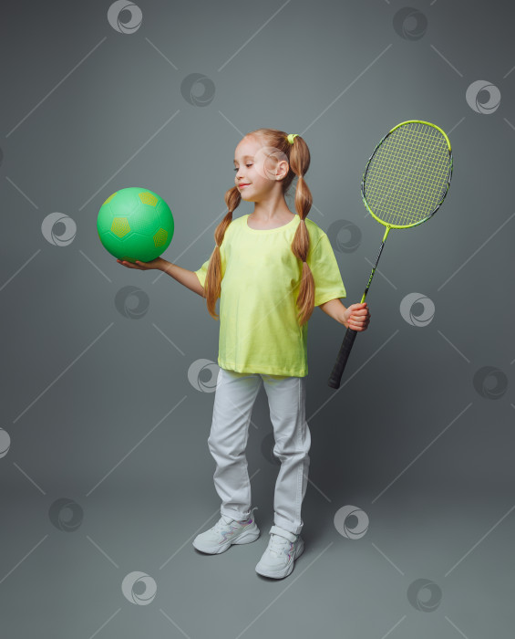 Скачать маленькая девочка держит мяч и ракетку на сером фоне. Концепция профессионального спорта. плакат на спортивную тематику, поздравительные открытки, заголовки.спорт фотосток Ozero