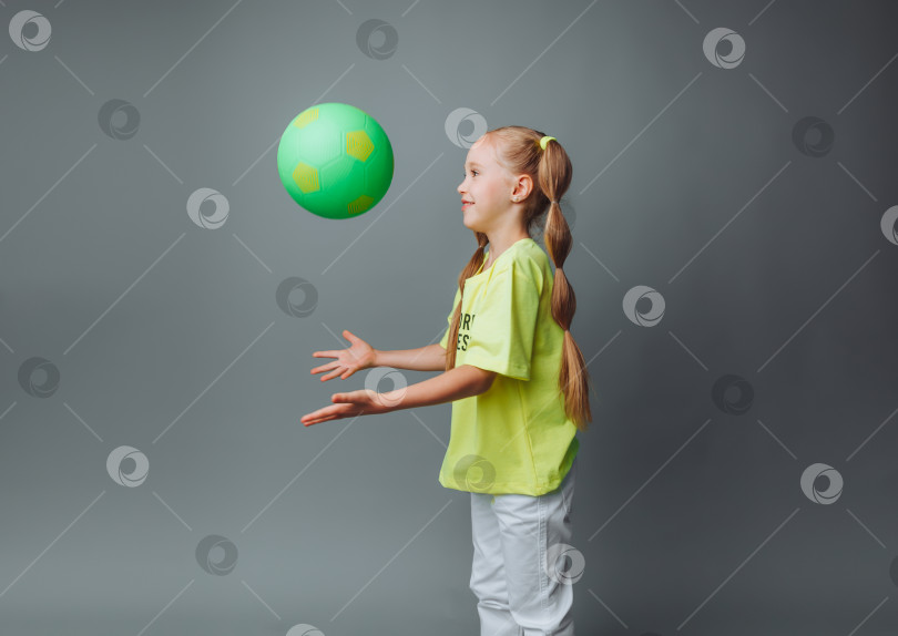 Скачать маленькая девочка подбрасывает мяч вверх, выделяясь на сером фоне. маленький спортсмен.детский спорт. фотосток Ozero