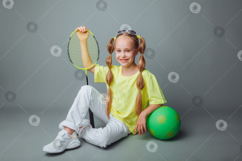 Скачать маленькая девочка сидит на сером фоне с ракеткой, мячом и спортивной сумкой. маленький спортсмен. детский спорт. спортивный контент. фотосток Ozero