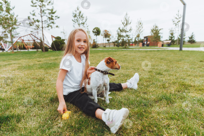 Скачать маленькая девочка целует и обнимает свою собаку Джек-рассел-терьера в парке. Любовь между хозяином и собакой. ребенок держит на руках собаку. фотосток Ozero
