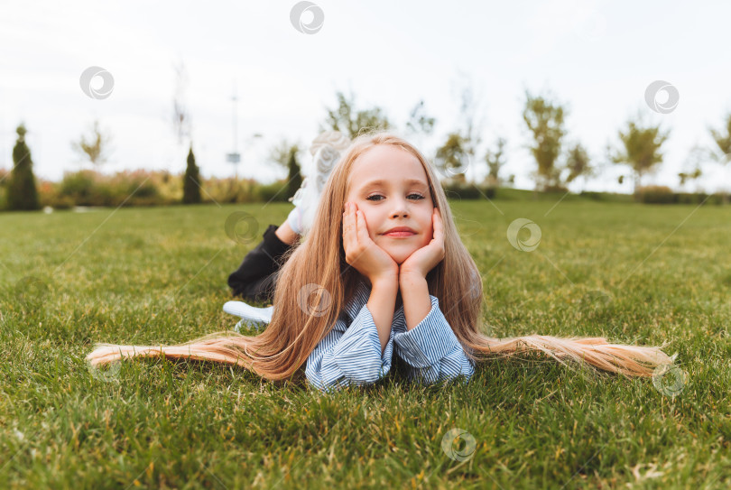 Скачать Счастливая маленькая девочка в джинсовой куртке лежит на зеленой траве газона. улыбающийся ребенок отдыхает, лежа на траве. концепция беззаботного детства. фотосток Ozero