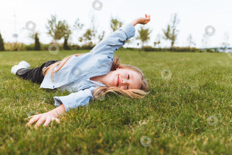Скачать Счастливая маленькая девочка в джинсовой куртке лежит на зеленой траве газона. улыбающийся ребенок отдыхает, лежа на траве. концепция беззаботного детства. фотосток Ozero