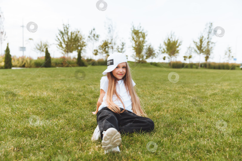 Скачать Милая, счастливая маленькая девочка, сидящая на траве в парке. Смеется, наслаждается свежим воздухом. ребенок сидит на траве фотосток Ozero