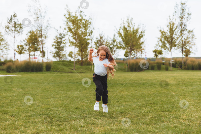 Скачать маленькая веселая девочка с длинными волосами бегает по траве в парке и радуется. фотосток Ozero