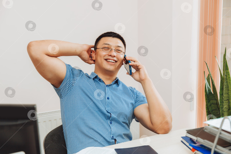 Скачать молодой азиатский бизнесмен разговаривает по телефону, чтобы обсудить работу в офисе. этот мужчина - азиат. фотосток Ozero