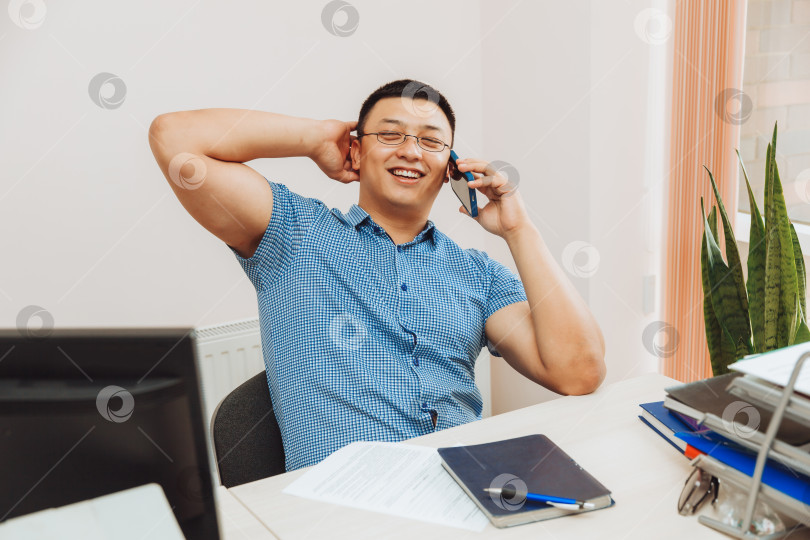 Скачать молодой азиатский бизнесмен разговаривает по телефону, чтобы обсудить работу в офисе. этот мужчина - азиат. фотосток Ozero