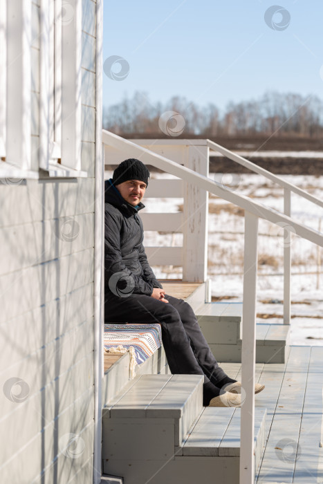 Скачать Мужчина сидит на крыльце дома зимним утром, эа фотосток Ozero