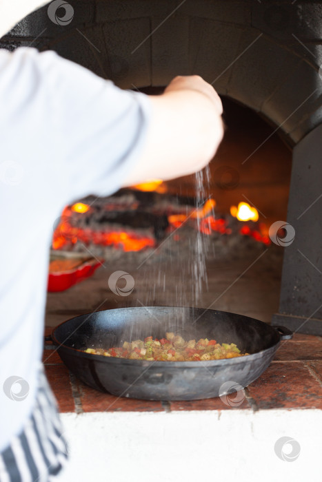 Скачать Повар солит овощи, которые томятся в чугунной сковороде фотосток Ozero