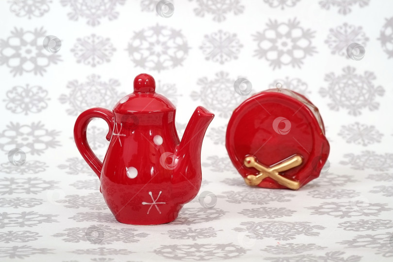Скачать Красные керамические рождественские игрушки (маленький чайник и барабан), выложенные на рождественскую скатерть снежинками фотосток Ozero