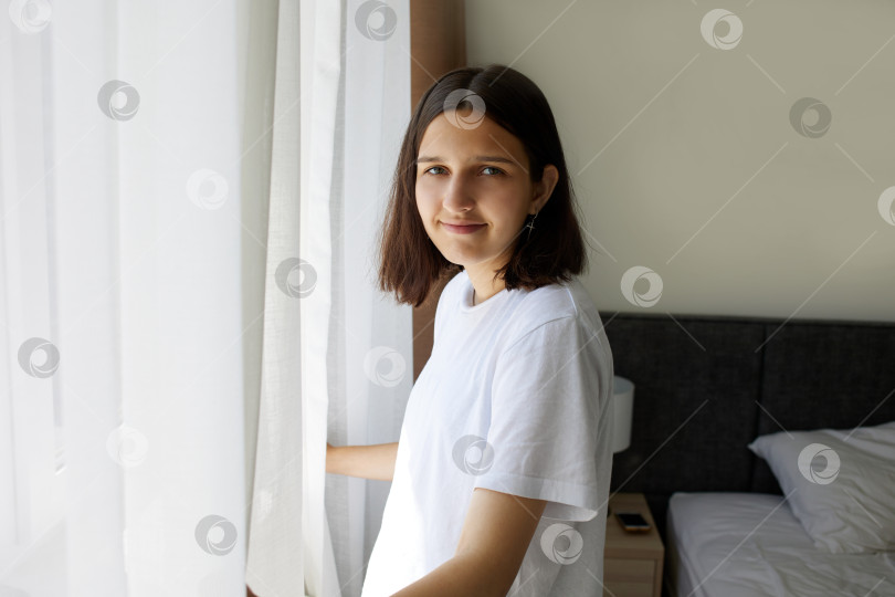 Скачать Молодая девушка стоит в спальне у окна. фотосток Ozero