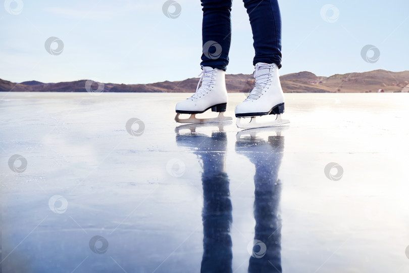 Скачать Женские ножки в белых коньках на открытом катке на закате. Молодая женщина катается верхом по замерзшему озеру Байкал. фотосток Ozero