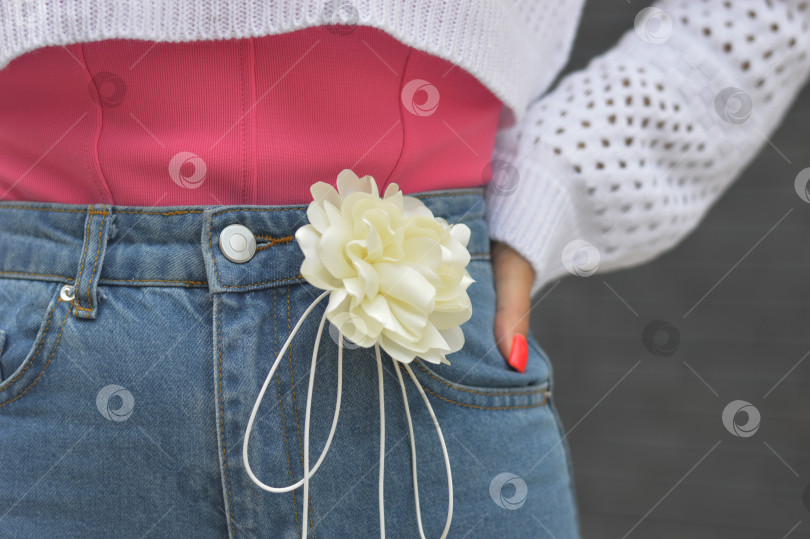 Скачать Красивый белый декоративный цветок на синих джинсах молодой стройной женщины крупным планом. Стильный декоративный элемент. фотосток Ozero