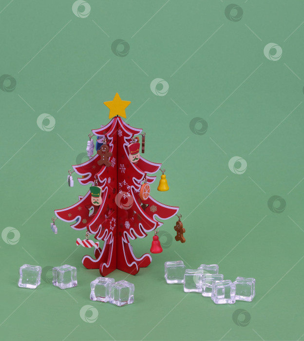 Скачать Изолированная красная деревянная рождественская елка и кусочки игрушечного льда на зеленом фоне фотосток Ozero