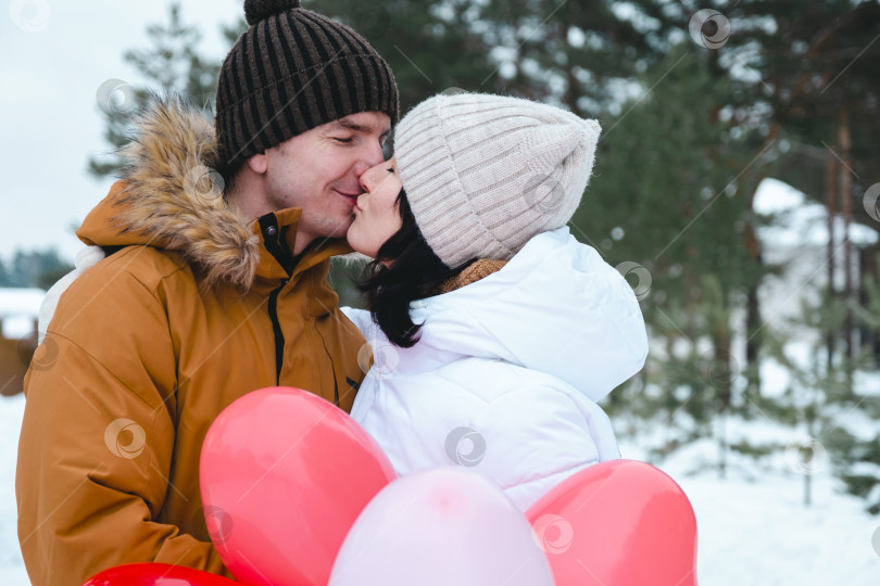 Скачать Влюбленные мужчина и женщина целуются на свидании на открытом воздухе зимой в снегу с подарком из розовых и красных воздушных шаров в форме сердца. День Святого Валентина, любовь, счастливая влюбленная пара на прогулке фотосток Ozero