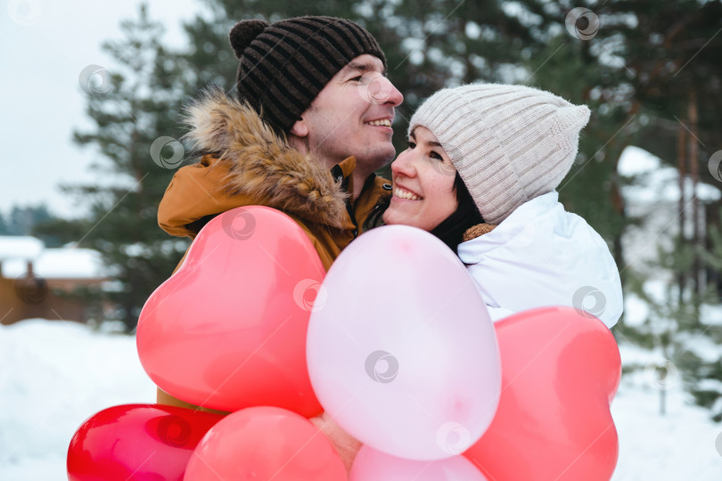 Скачать Влюбленные мужчина и женщина на свидании на открытом воздухе зимой, в снегу, с подарком из розовых и красных воздушных шаров в форме сердца. День Святого Валентина, любовь, счастливая влюбленная пара на прогулке фотосток Ozero