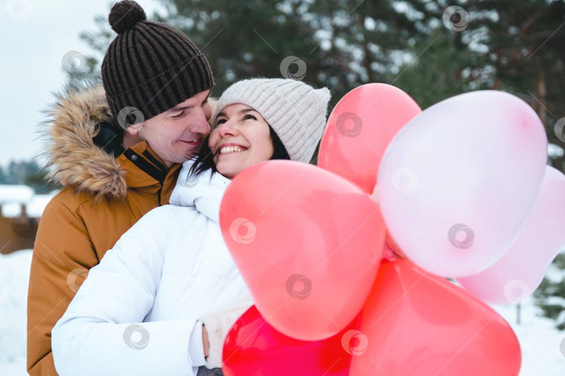 Скачать Влюбленные мужчина и женщина на свидании на открытом воздухе зимой в снегу с подарком из розовых и красных воздушных шаров в форме сердца. День святого Валентина, любовь, счастливая влюбленная пара на прогулке фотосток Ozero
