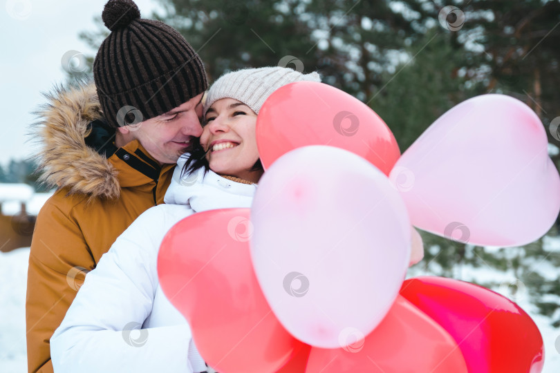 Скачать Влюбленные мужчина и женщина на свидании на открытом воздухе зимой в снегу с подарком из розовых и красных воздушных шаров в форме сердца. День святого Валентина, любовь, счастливая влюбленная пара на прогулке фотосток Ozero