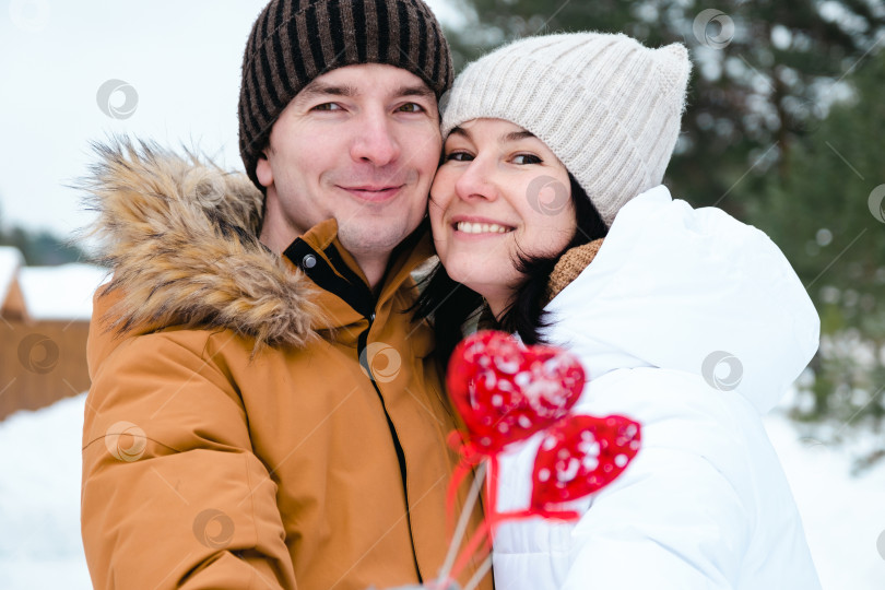 Скачать Влюбленные мужчина и женщина на свидании на открытом воздухе зимой в снегу с красным декором в форме сердца. День святого Валентина, любовь, счастливая влюбленная пара на прогулке, объятия и поцелуи фотосток Ozero