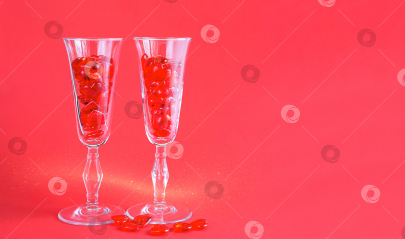 Скачать Два бокала для шампанского наполнены стеклянными сердечками на красном фоне с пробелом для текста. День святого Валентина, любовь, романтическое свидание фотосток Ozero