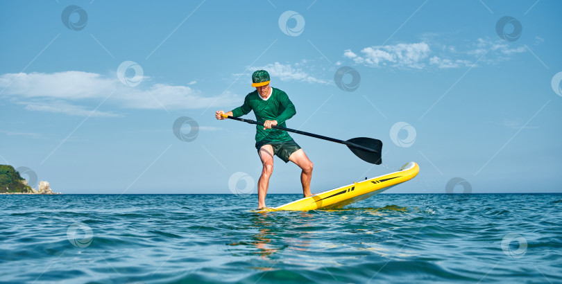 Скачать Спортсмен на большом желтом SUP с веслом выполняет поворотный трюк в бирюзовой воде. Активный отдых. фотосток Ozero