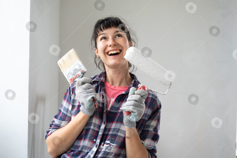 Скачать Портрет счастливой женщины с малярным валиком и белой краской для стен в руках крупным планом. Строительные работы и косметический ремонт в доме, покраска стен, тонировка, отделочные работы своими руками фотосток Ozero
