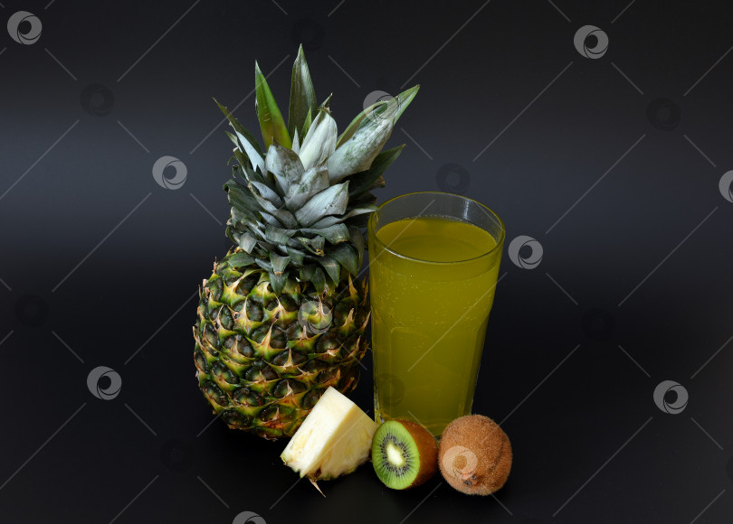Скачать Высокий граненый стакан с освежающим соком из тропических фруктов на черном фоне, рядом с кусочками спелого киви и ананаса. фотосток Ozero