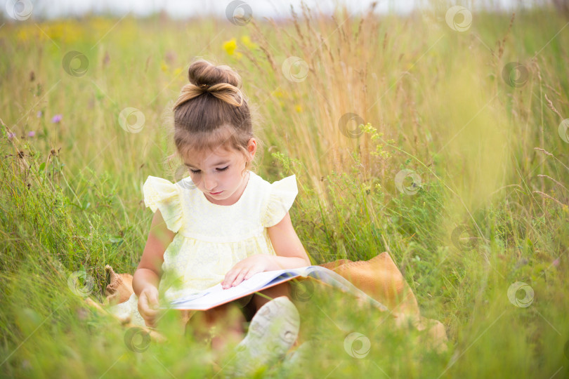 Скачать Девушка в желтом платье сидит в траве на одеяле в поле и читает бумажную книгу. Международный день защиты детей. Летнее время, детство, образование и развлечения, ядро коттеджа. Пространство для копирования фотосток Ozero
