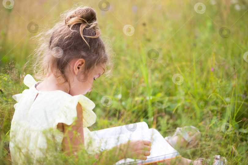 Скачать Девушка в желтом платье сидит в траве на одеяле в поле и читает бумажную книгу. Международный день защиты детей. Летнее время, детство, образование и развлечения, ядро коттеджа. Пространство для копирования фотосток Ozero