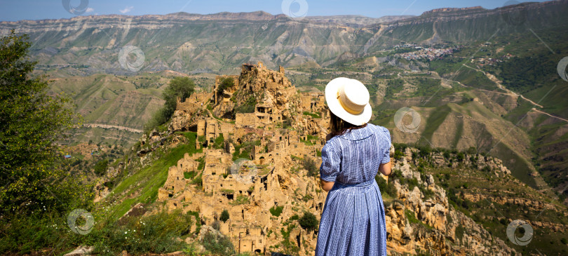 Скачать Туристка высоко в горах Дагестана любуется захватывающим панорамным видом на природу и древний заброшенный город Гамсутль. Кавказские горы, туристическая достопримечательность, руины, треккинговый тур фотосток Ozero